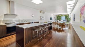 Une cuisine moderne dotée d’un îlot central, de tabourets de bar et d’un coin repas offrant une vue sur la verdure.