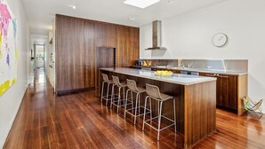 Une cuisine moderne dotée d’un îlot central, de tabourets de bar, de meubles en bois et d’une hotte en acier inoxydable.