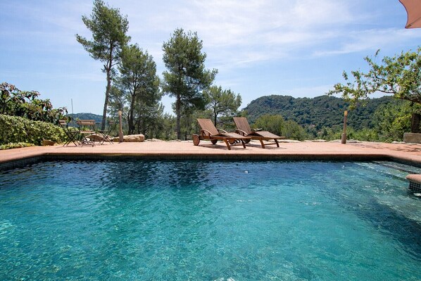 A clear blue pool with lounge chairs and a view of a forested hill.