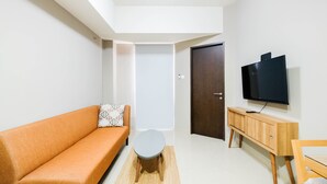 A living room with a sofa, a small table, a TV on a wooden stand, and a door in the background.