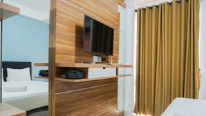 Una habitación de hotel moderna con una cama, un televisor fijado a un panel de madera, una mesita y una cortina.