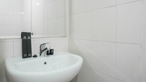 Un lavabo de baño blanco con un espejo encima, un grifo y dos cepillos de dientes con un tubo de pasta dental sobre el lavabo.