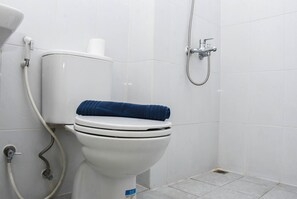 Sanitário branco com uma toalha azul sobre a tampa, um rolo de papel higiénico e um chuveiro.