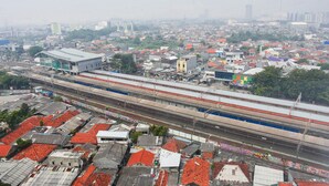 Un treno ad alta velocità che attraversa una zona urbana densamente popolata con diverse linee ferroviarie e un'ampia stazione.