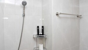 Un espace douche équipé d’un pommeau de douche à main, d’une barre pour les serviettes et d’une étagère pour les articles de toilette.