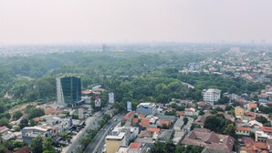 Un paysage urbain avec un bâtiment moderne imposant, un mélange de bâtiments résidentiels et commerciaux, et une vaste zone verdoyante au premier plan.