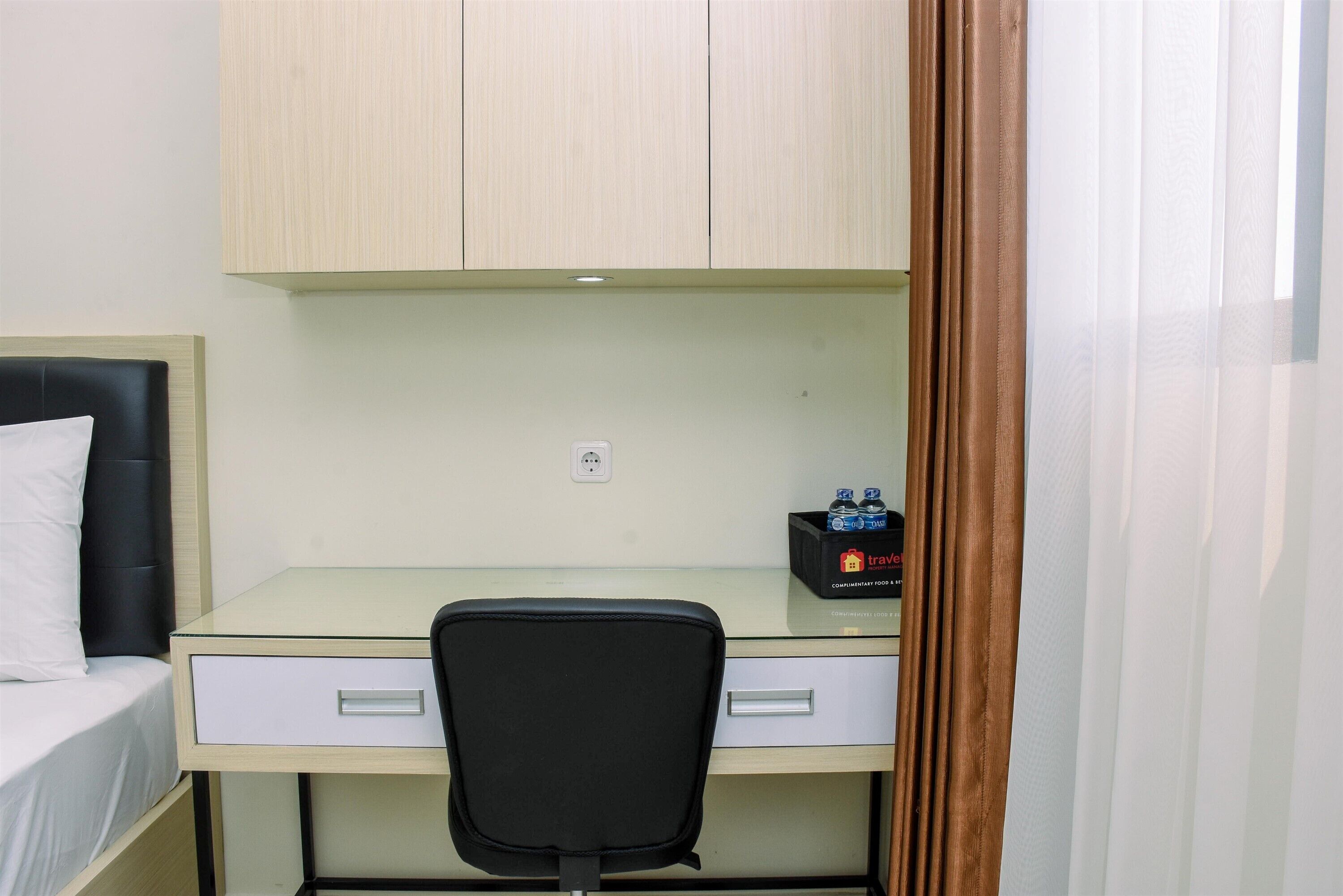A compact room with a bed, a desk with a chair, a small cabinet, and a power outlet.