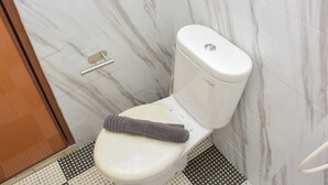 A toilet with a towel on the seat, a toilet paper holder, and a patterned floor.