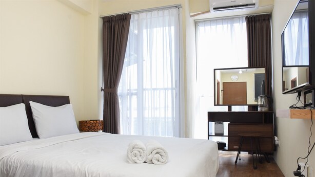 A hotel room with a bed, a desk, a chair, a mirror, and a window with curtains.