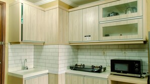 A compact kitchen with wooden cabinets, a microwave, and a gas stove. - Minimalist And Comfort Living 2Br At Signature Park Grande Apartment (Jakarta)