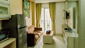 A compact living space with a sofa, a coffee table, a TV, and a refrigerator. - Minimalist And Comfort Living 2Br At Signature Park Grande Apartment (Jakarta)