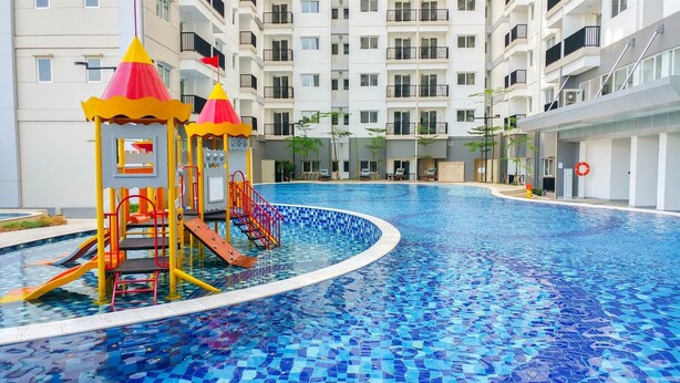 A swimming pool with a slide and a play structure, surrounded by a building with balconies and a tiled floor. - Minimalist And Comfort Living 2Br At Signature Park Grande Apartment (Jakarta)