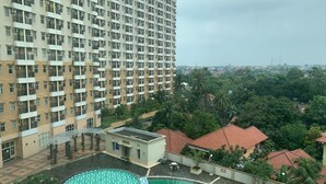 A high-rise residential building with multiple balconies, a swimming pool, and surrounding greenery. - Comfort Living Studio At Margonda Residence 1 Apartment (Depok)