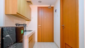 A narrow hallway with a wooden door and a small kitchenette area with a sink and cabinets. - Simply And Comfort Living Studio Room At Margonda Residence 3 Apartment (Depok)
