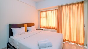 A neatly made bed with white linens and two folded towels, a wooden headboard, and a nightstand with a lamp. - Simply And Comfort Living Studio Room At Margonda Residence 3 Apartment (Depok)
