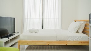 Een slaapkamer met een houten bed, witte beddengoed, een televisie op een standaard en een raam met dunne gordijnen.