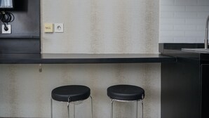 A kitchen with a black countertop, two bar stools, a sink, and a wall-mounted electrical outlet. - Nice And Cozy Studio At Bintaro Icon Apartment (South Tangerang)
