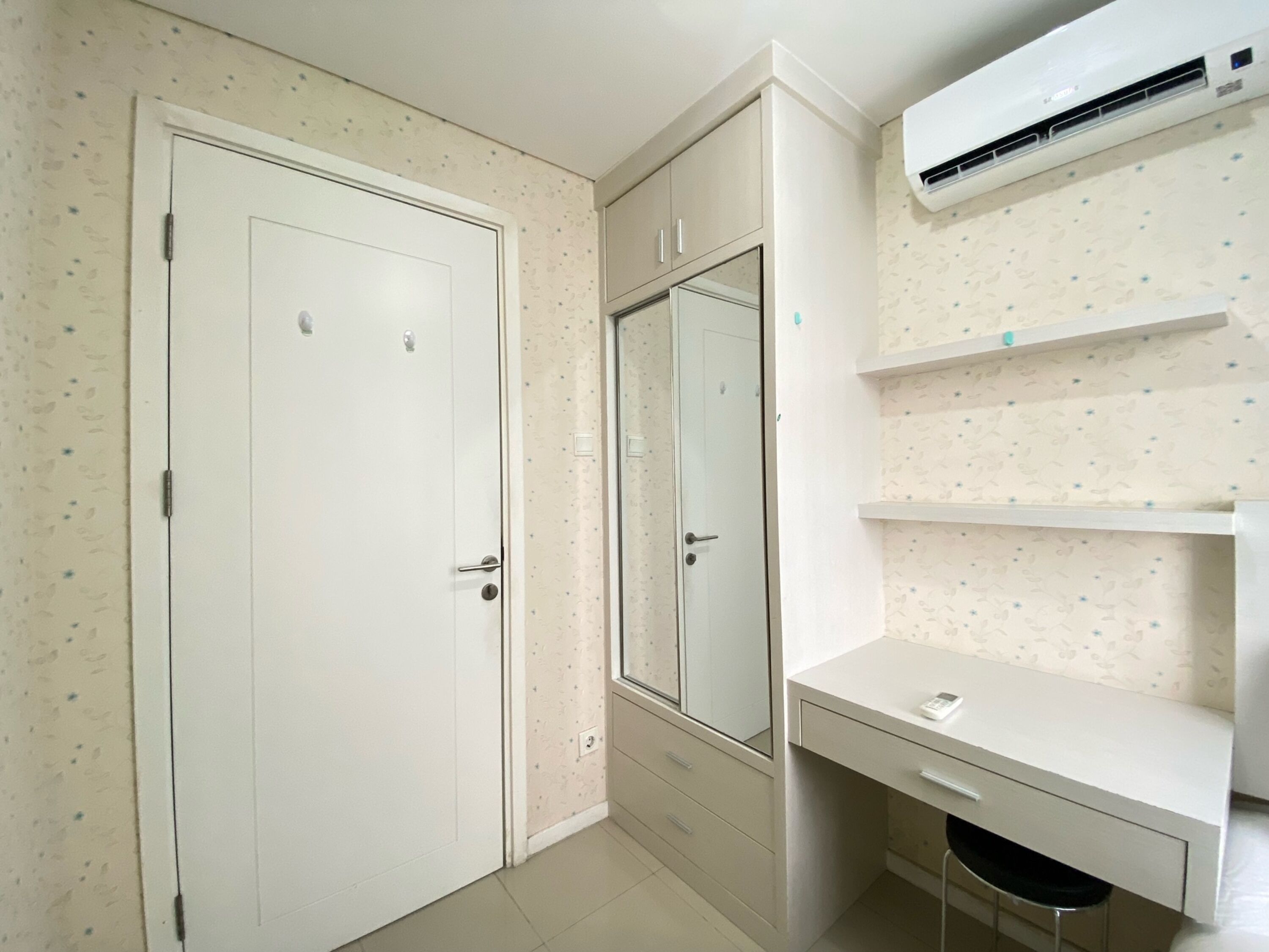 A room with a white door, a wardrobe, a mirror, a desk, and a wall-mounted air conditioner.