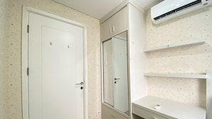 Una habitación con una puerta blanca, un armario, un espejo, un escritorio y un aire acondicionado instalado en la pared.