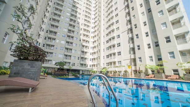 Un edificio residencial alto con piscina, mobiliario exterior y zonas verdes.