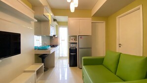 Una cocina compacta con televisor de pantalla plana, un sofá verde y un refrigerador.