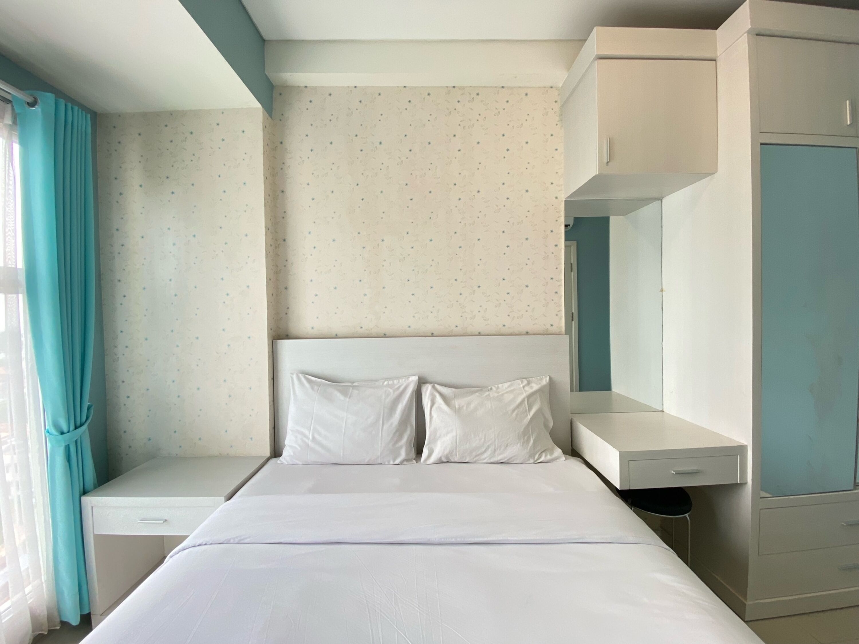 Une chambre à coucher comprenant un lit, une table de chevet, une armoire et une fenêtre avec des rideaux.