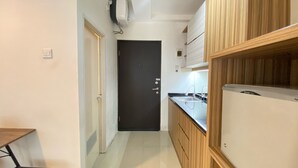 A narrow kitchen with wooden cabinets, a black door, and a small countertop with a sink. - Artsy Private Studio Room At Grand Asia Afrika Bandung Apartment (Bandung)