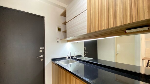 A modern kitchen with a black countertop, wooden cabinets, and a stainless steel sink. - Artsy Private Studio Room At Grand Asia Afrika Bandung Apartment (Bandung)