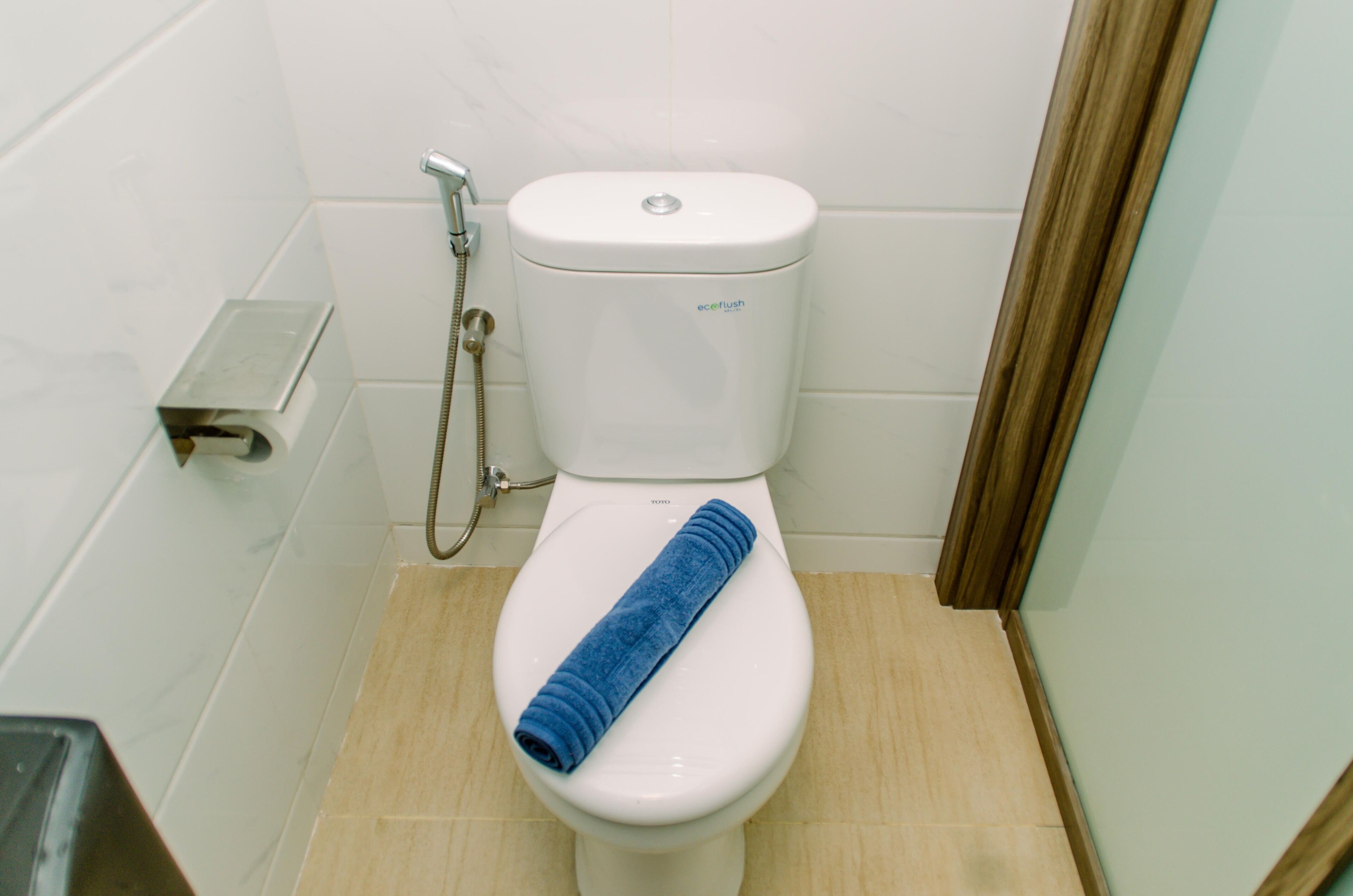 Toilette mit blauem Handtuch, Toilettenpapierhalter und Duschkopf.