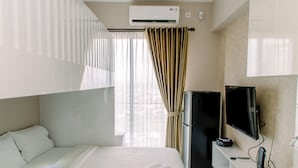 A hotel room with a bed, a television, a desk, and an air conditioning unit.