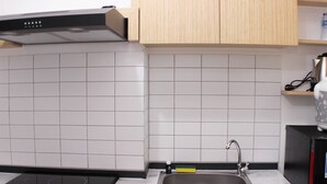 A modern kitchen with white tiles, a stainless steel sink, and a black induction cooktop. - Cozy And Nice Studio At Sayana Bekasi Apartment (Tarumajaya)