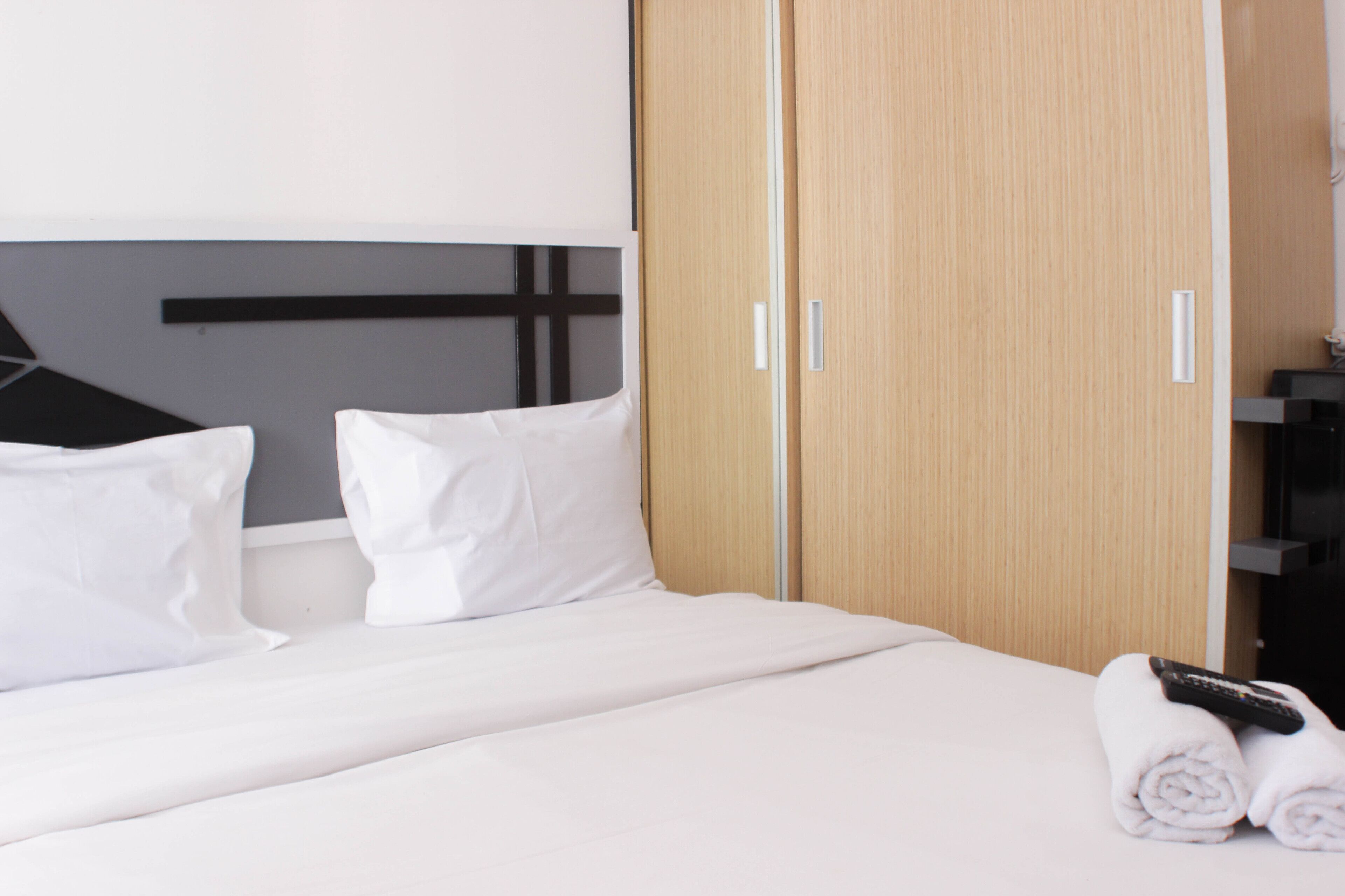 Een hotelkamer met een bed, witte kussens, een houten kledingkast en een afstandsbediening op een handdoek.