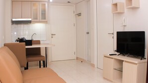A compact living space with a sofa, a TV on a wooden stand, a kitchen area with cabinets and a sink, and a door leading to another room. - Nice And Comfy 2Br Springlake Apartment Near Summarecon Bekasi (Bekasi)