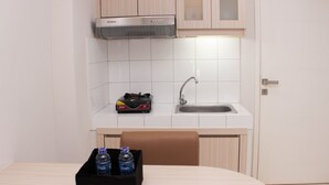 A small kitchenette with a gas stove, a sink, and a cabinet above the stove. There is a table with a box containing bottled water and a bottle. - Nice And Comfy 2Br Springlake Apartment Near Summarecon Bekasi (Bekasi)