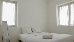 A minimalist bedroom with a single bed, white linens, and a small bedside table. - Spacious And Elegant 3Br At Grand Palace Kemayoran Apartment (Jakarta)