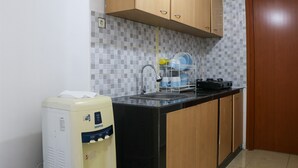 A kitchen with wooden cabinets, a black countertop, a dish rack, and a water dispenser. - Spacious And Elegant 3Br At Grand Palace Kemayoran Apartment (Jakarta)