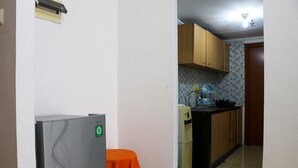 A compact kitchen with wooden cabinets, a refrigerator, and a small table with an orange tablecloth. - Spacious And Elegant 3Br At Grand Palace Kemayoran Apartment (Jakarta)