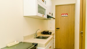 A compact kitchen with a microwave, sink, and a small countertop. A wooden door with a sign is visible in the background. - Warm And Cozy Studio Room Apartment At B Residence (Pagedangan)