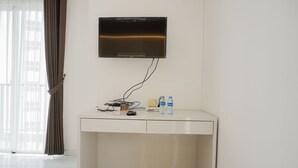 A modern hotel room with a flat-screen TV mounted on the wall, a desk with a remote control, and two water bottles on the counter. - Elegant And Restful Studio At Casa De Parco Apartment (South Tangerang)