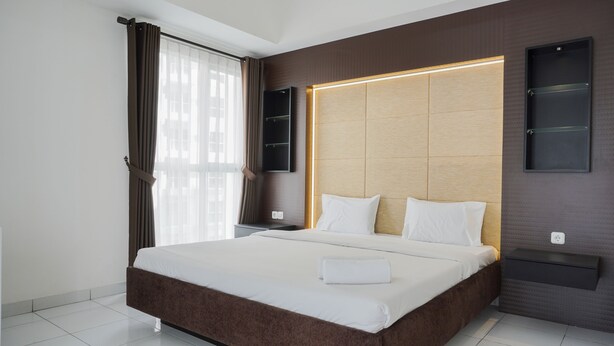 A modern hotel room with a large bed, a wooden headboard, a bedside table, and a wall-mounted shelf. - Elegant And Restful Studio At Casa De Parco Apartment (South Tangerang)