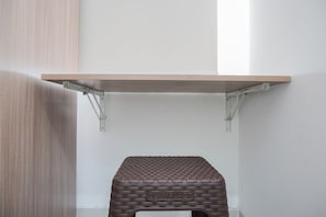 Simple, functional room with a light-colored wall and a shelf, featuring a brown stool.