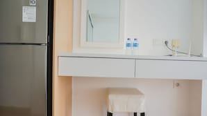 A compact kitchen with a refrigerator, a small stool, and a countertop with two water bottles. - Nice And Cozy Studio Room At Casa De Parco Apartment (Pagedangan)