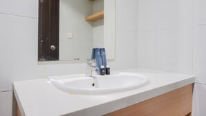 A bathroom with a white sink, a mirror, and two blue bottles on the counter. - Nice And Cozy Studio Room At Casa De Parco Apartment (Pagedangan)