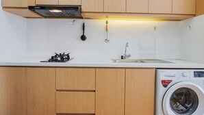 A kitchen with wooden cabinets, a stove, a sink, and a washing machine. - Nice And Cozy Studio Room At Casa De Parco Apartment (Pagedangan)