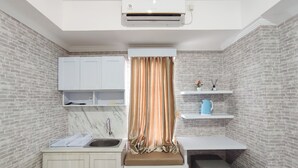 A compact kitchen with a built-in sink, white cabinets, a marble countertop, a black refrigerator, and a window with a curtain.
