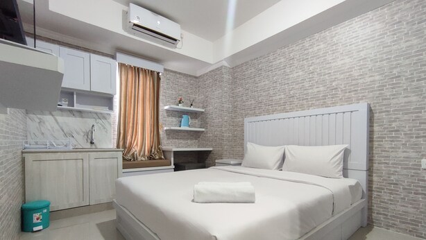 A modern hotel room with a large bed, a built-in wardrobe, a kitchen area, and a brick wall.