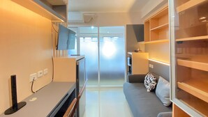 A modern living room with a flat-screen TV, a desk with a computer, a sofa, and a glass door leading to a balcony. - Minimalist And Nice 1Br At Gateway Pasteur Apartment (Cimahi)
