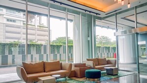 A modern lobby with large windows, a beige sofa set, and a small round table. - Elegant And Nice 1Br At The Smith Alam Sutera Apartment (Tangerang)