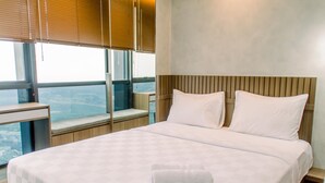 A hotel room with a large bed, a window with a view, a bedside table, and a wooden headboard. - Elegant And Nice 1Br At The Smith Alam Sutera Apartment (Tangerang)