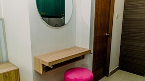 A room with a wooden cabinet, a pink stool, a mirror, and a wooden door. - Nice And Simply Studio At Amazana Serpong Apartment (South Tangerang)